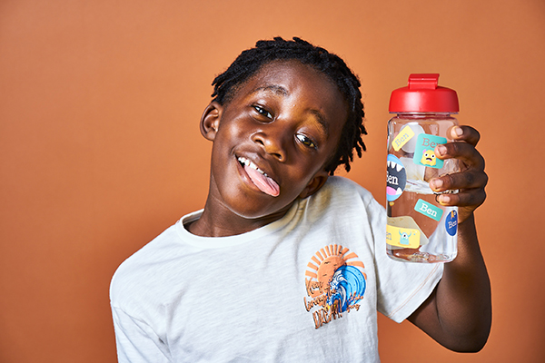 Boy holding a water bottle with waterproof name stickers from My Nametags, on a brown background